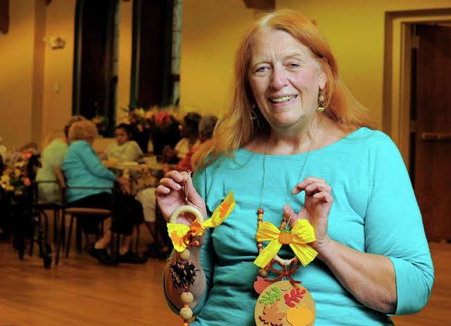 Elizabeth Betty McOsker, Program Administrator, holding fall-themed crafts at the Over 60 Club